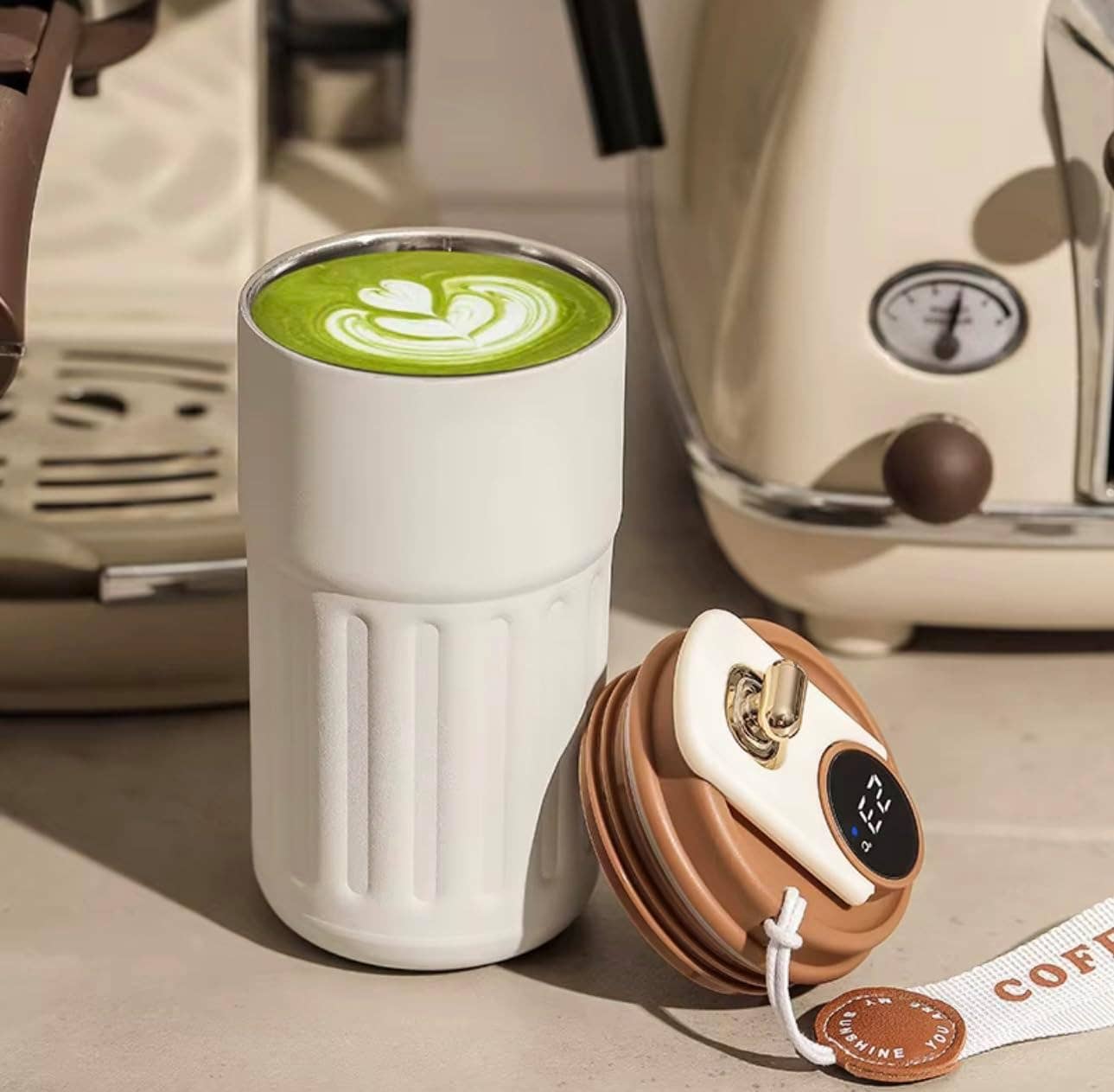 White thermos with green drink and brown lid on a surface with a coffee machine in the background