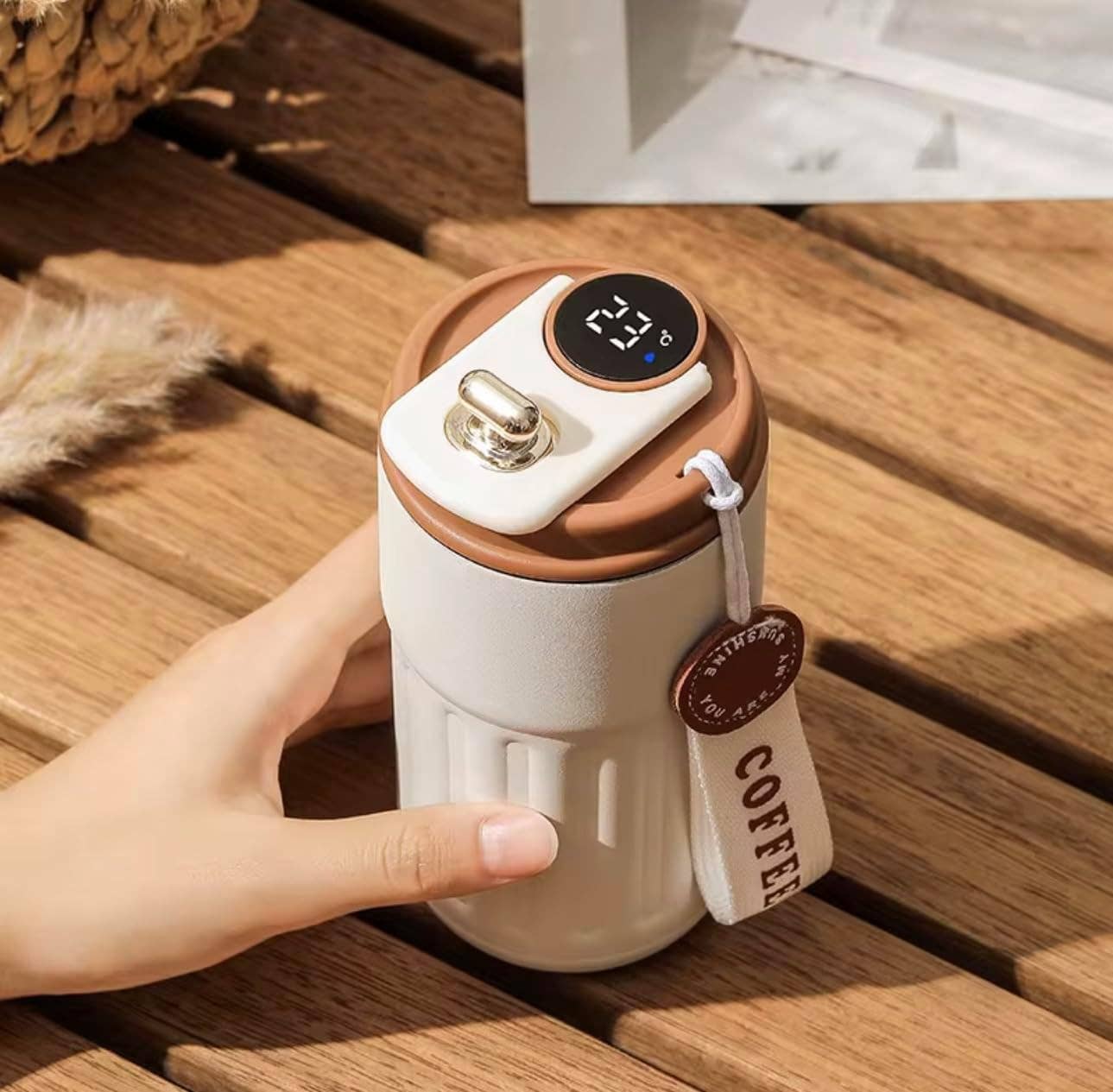 Hand holding a white and brown coffee maker on a wooden surface