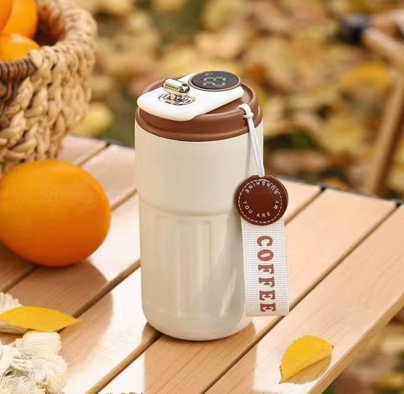 White and brown travel mug with a tag on a wooden surface with oranges and leaves.