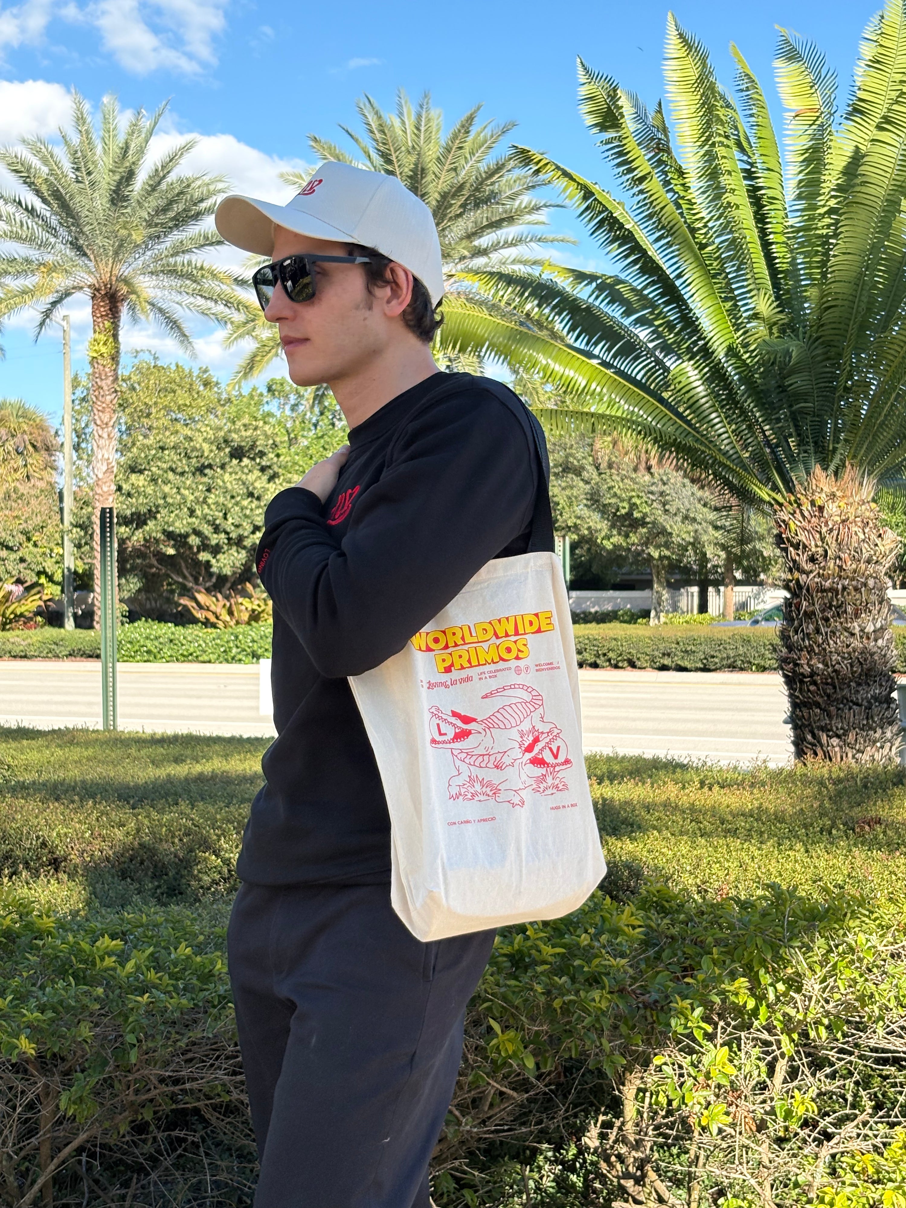 Person holding a tote bag with text and graphics, standing outdoors with palm trees in the background