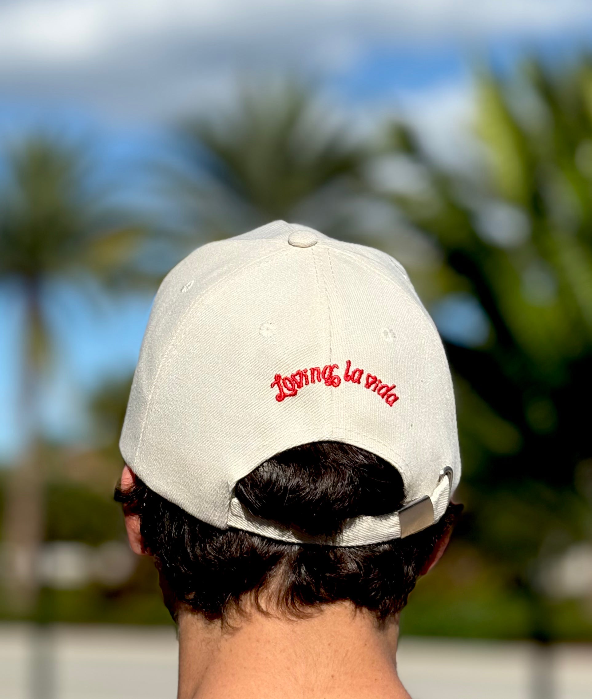 Person wearing a cap with 'Living la vida' text against a blurred outdoor background