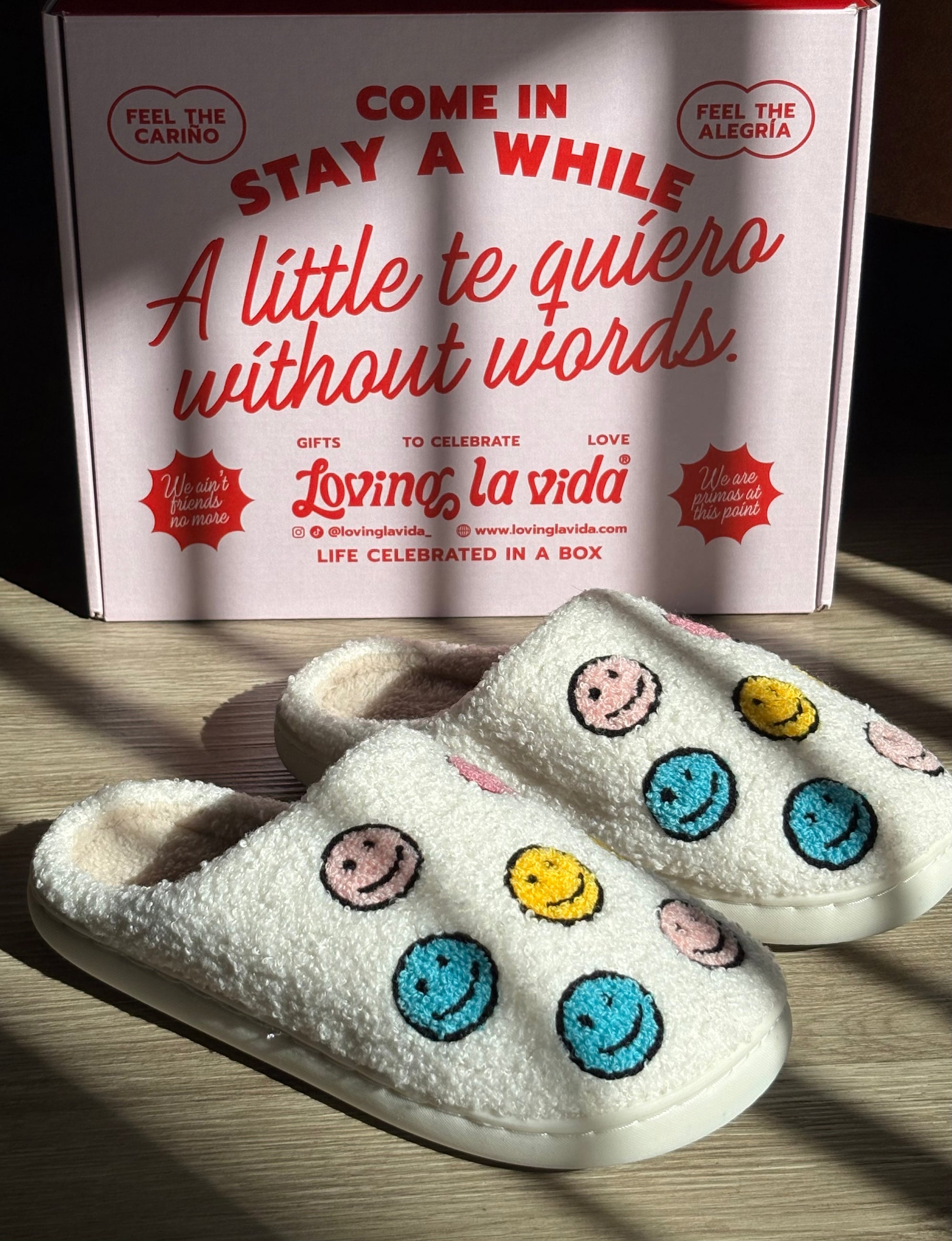 White slippers with colorful smiley face patterns in front of a promotional box.