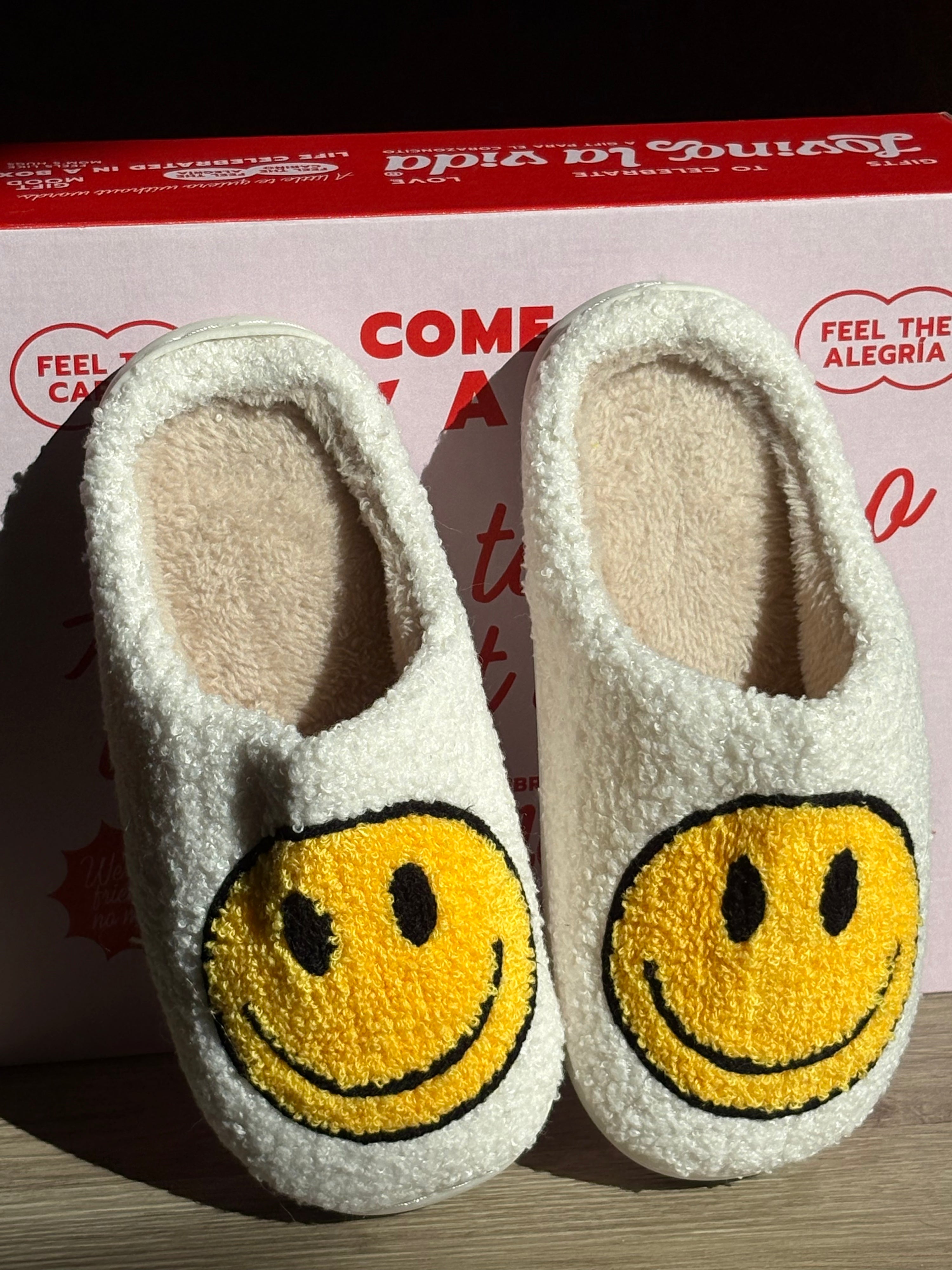 White slippers with yellow smiley face design on a branded box background